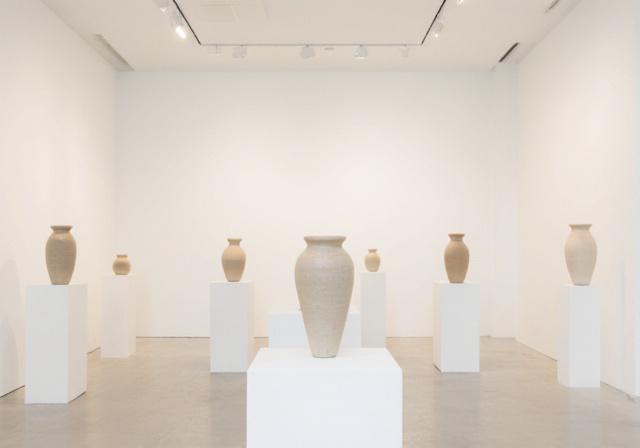 An airy ceramic gallery space with finished pottery on white pedestals